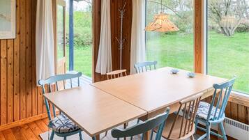 A wooden dining table with chairs, a hanging light fixture, and a view of a garden through large windows.