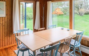 Ein Holztisch mit Stühlen, eine Hängeleuchte und Blick auf einen Garten durch große Fenster.