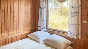 Une chambre dans un chalet en bois, avec un lit, deux oreillers et une fenêtre avec des rideaux.