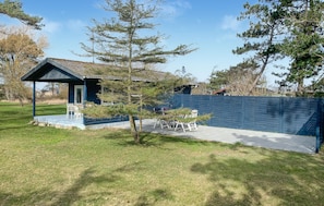 Ein Haus mit überdachter Terrasse, umzäunter Garten und kleinem Gartenbereich.