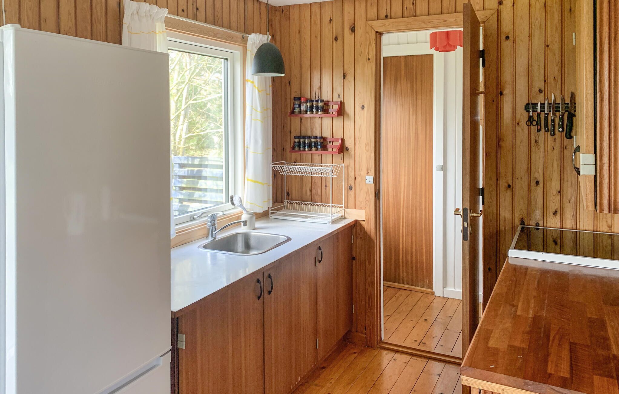 Une cuisine de taille réduite, avec des meubles en bois, un réfrigérateur blanc, un évier et une fenêtre.