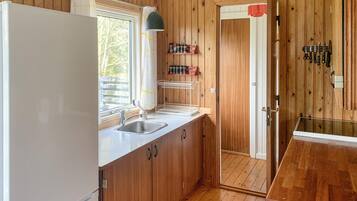 Une cuisine de taille réduite, avec des meubles en bois, un réfrigérateur blanc, un évier et une fenêtre.