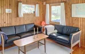 Ein Zimmer mit Holzwänden, zwei schwarzen Ledersofas, einem Holztisch und einem kleinen Tisch mit einer Kerze.