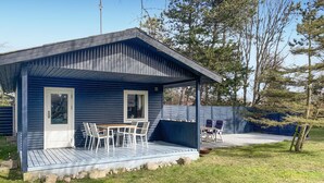 Une petite cabane bleue avec une véranda, deux fenêtres et une table avec des chaises.
