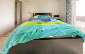Ein Bett mit einer farbenfrohen Stegdecke, einer Nachttischlampe und einem Fenster mit Vorhängen.