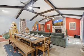 Comedor con mesa de madera preparada para cuatro personas, un sofá verde y una chimenea de piedra.