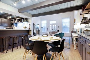 Una cocina moderna con taburetes de bar, una mesa de comedor preparada para cuatro personas y una escalera que sube a un nivel superior.