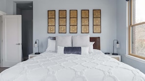 Un dormitorio con una cama grande, una mesita de noche con una lámpara, una luz de pared y una ventana.