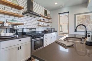 Una cocina moderna con armarios blancos, estufa de acero inoxidable y un ventanal grande.