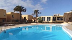 Une piscine à l’eau d’un bleu cristallin, entourée d’une terrasse carrelée, de palmiers et d’immeubles dotés de grandes fenêtres.