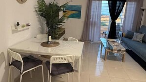 Un coin repas comprenant une table, des chaises, une horloge, une plante et un tableau accroché au mur.