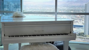 Un pianoforte a coda in un'ampia stanza con vista sulla città, un lampadario decorativo e un piccolo sgabello bianco.