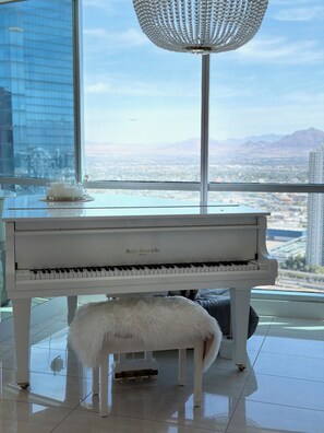 A grand piano in a spacious room with a city view, a decorative chandelier, and a small white stool. - Spacious 3-bedroom condo in amazing Las Vegas with AC and gym (Las Vegas)