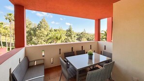 Ein überdachter Außenbereich mit Tisch und Stühlen, Blick auf Bäume und Hügel, und eine rote Decke.