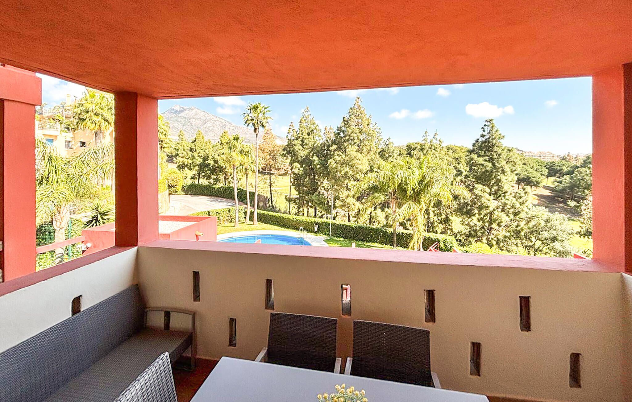 A balcony with a view of a pool, greenery, and a mountain.