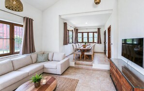 Un salon moderne avec un canapé, un coin repas, un téléviseur et de grandes fenêtres.