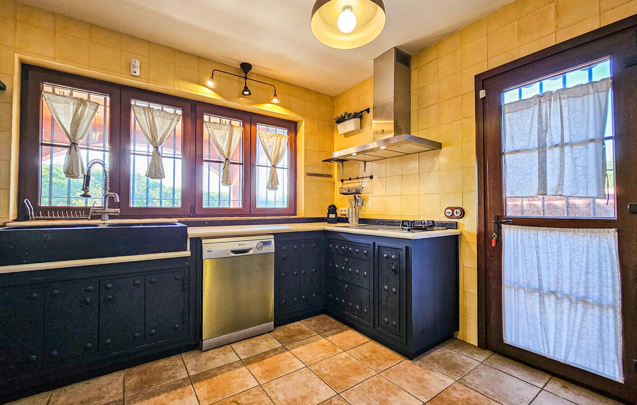 A kitchen with a dishwasher, stove, and large windows with curtains.