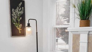 A room with a blue sofa, a small round table with a magazine, a floor lamp, and a plant on a mantelpiece.