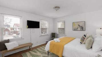 Ein Schlafzimmer mit einem Bett, einer Bank, einem Fernseher und einem Fenster mit Jalousien.