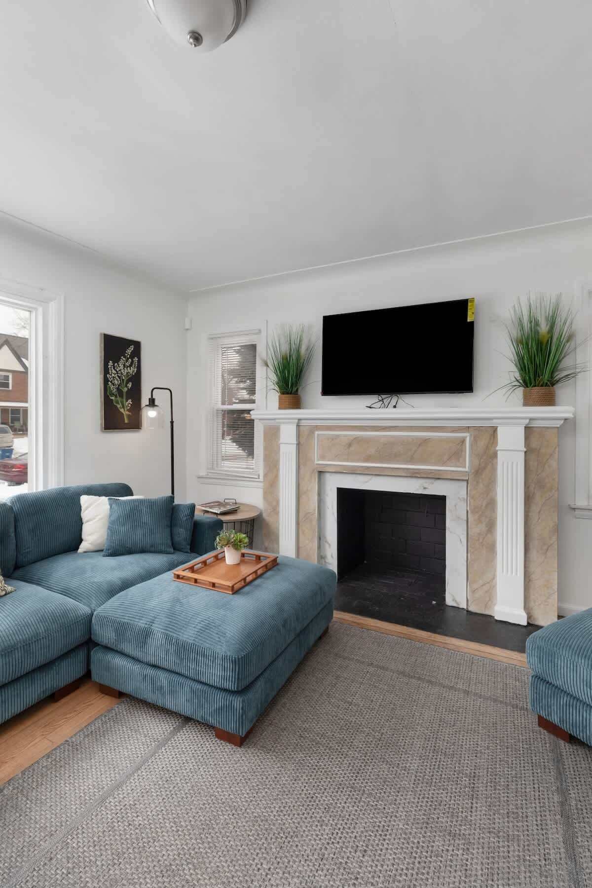 A living room with a sectional sofa, a fireplace, a mounted TV, and a potted plant.