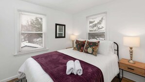 A bedroom with a bed, two bedside lamps, a nightstand, and a window with blinds.