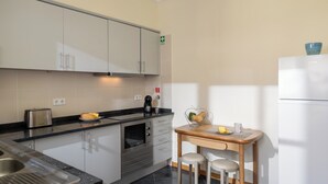 Et moderne køkken med indbygget ovn, kaffemaskine og et lille spisebord med barstole.