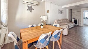 Un área de comedor con una mesa y sillas de madera, un sofá, un equipo de aire acondicionado y una decoración con forma de estrella de mar en la pared.
