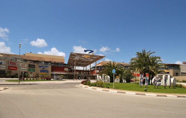 Zona comercial con una glorieta, un paso de peatones cubierto y diversas tiendas, incluyendo Levi's, Burger King y H&M.