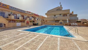 Una piscina con solárium de azulejos, un flotador salvavidas y una bandera en un edificio.
