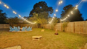 Ein Garten mit Holzzaun, Lichterketten, einem Feuerkorb und Gartenmöbeln.