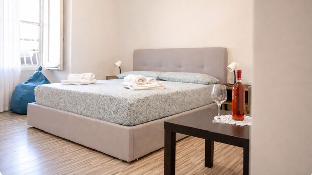 A bedroom with a bed, pillows, a bedside table with a wine bottle, a lamp, and a blue bean bag chair. - Vacation House - A Ridosso dei Sassi (Matera)