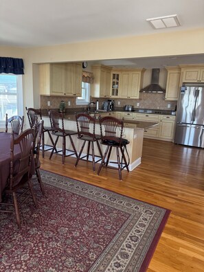 A spacious kitchen with wooden cabinets, a stainless steel refrigerator, and a dining area with a patterned rug. - Perfect Oceanfront Home with 5 Bedrooms in ideal Surf City with Central AC. (Surf City)