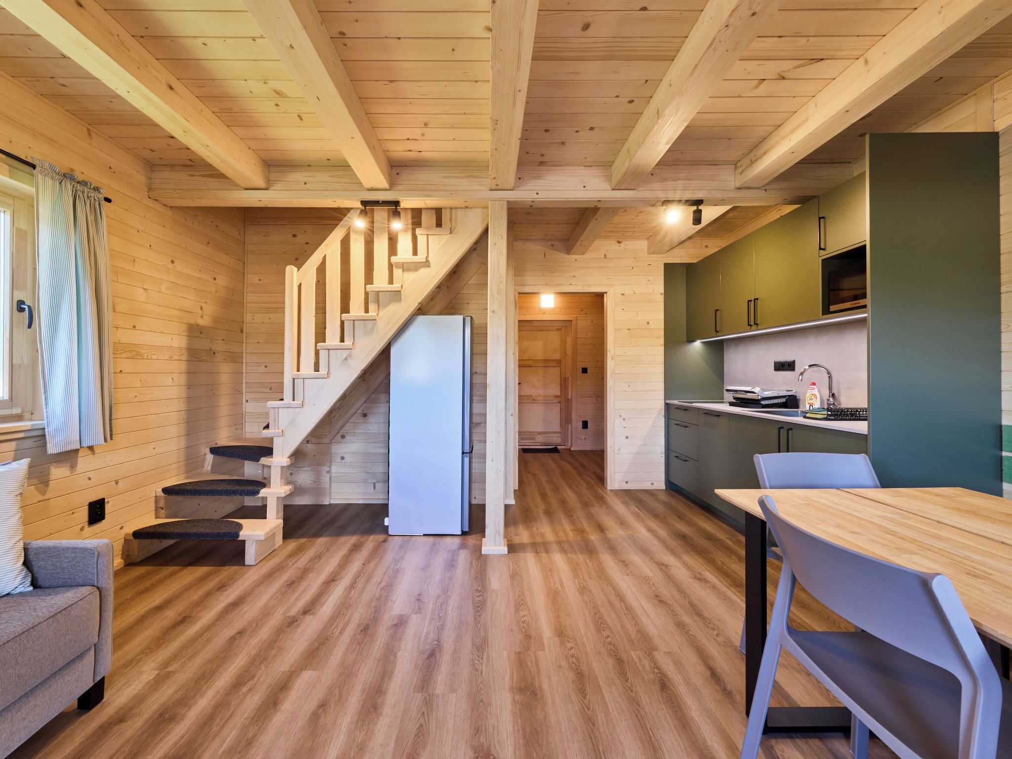 A wooden interior with a staircase, a refrigerator, a dining table, and a kitchen area.