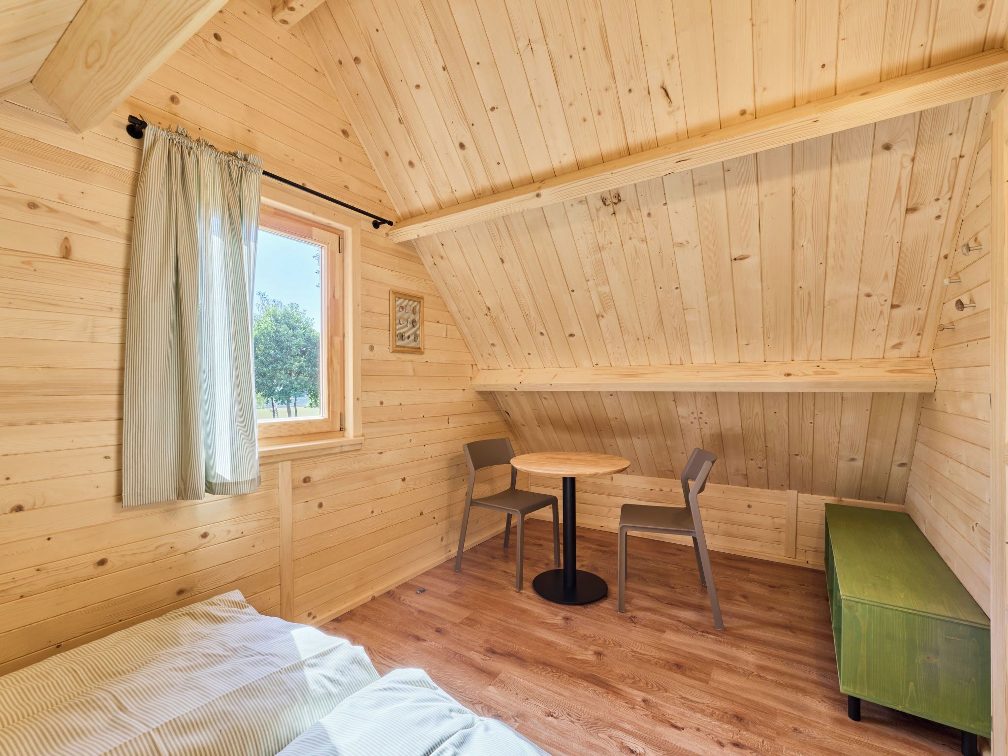 A cozy cabin with a wooden interior, a bed, a small table, two chairs, and a window with curtains.