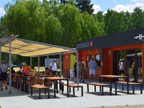 Ein Außenbereich mit Tischen und Bänken, ein überdachtes Pavillon und ein Restaurantgebäude mit einem Schild.