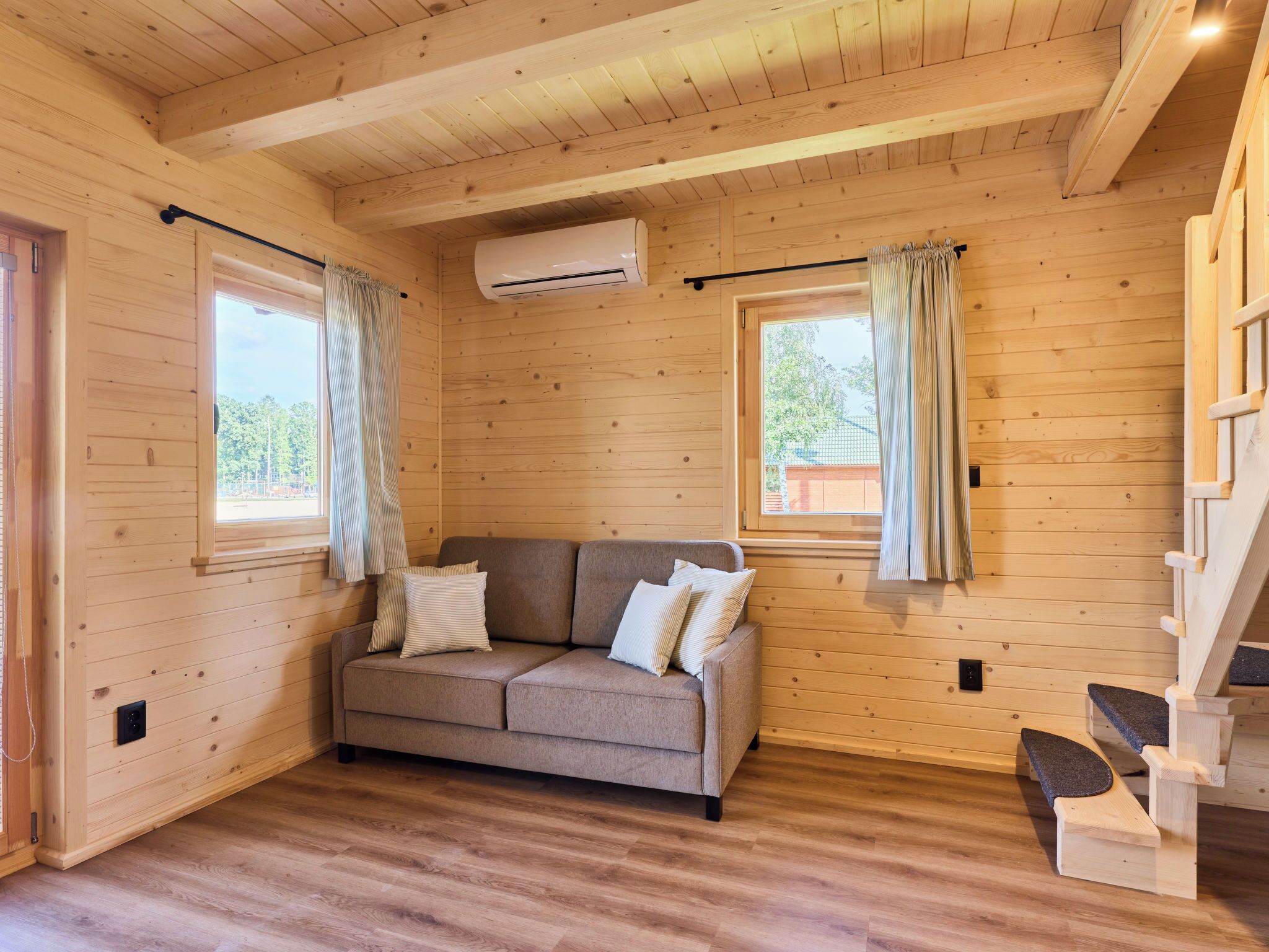 Interior acolhedor de uma cabana com piso de madeira, um sofá e uma escada.