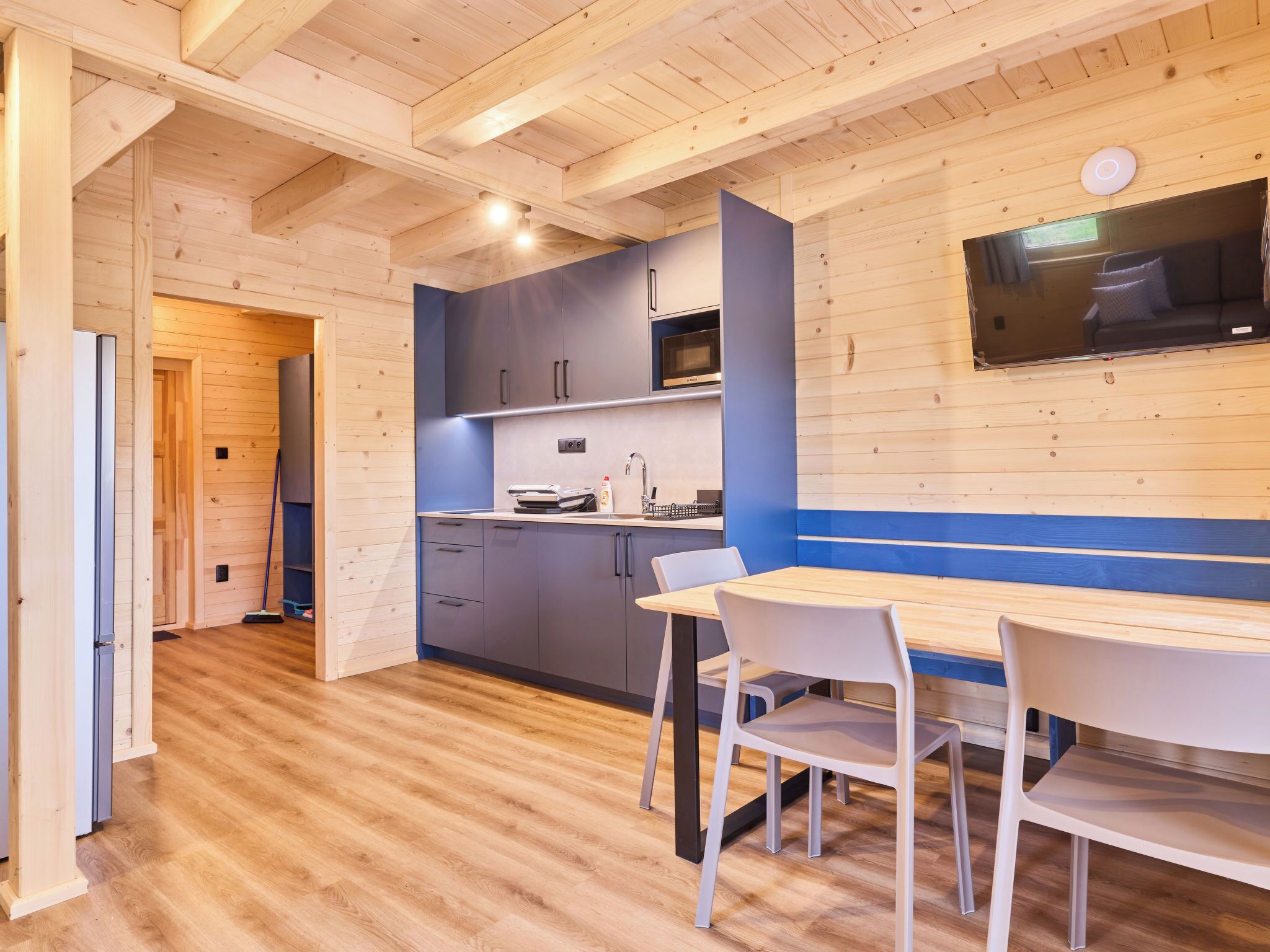 A modern kitchen with wooden beams, grey cabinets, and a blue accent wall.