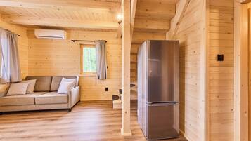 A wooden cabin interior with a sofa, a refrigerator, and a window with curtains.