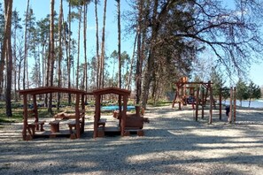 A playground with wooden structures and benches, surrounded by trees.