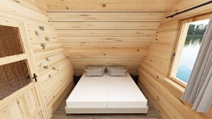 Een kleine houten kamer met een bed, een raam en een houten vloer.