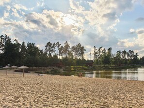 Ein Strand mit Sand, Sonnenschirmen, einem See und Bäumen im Hintergrund.