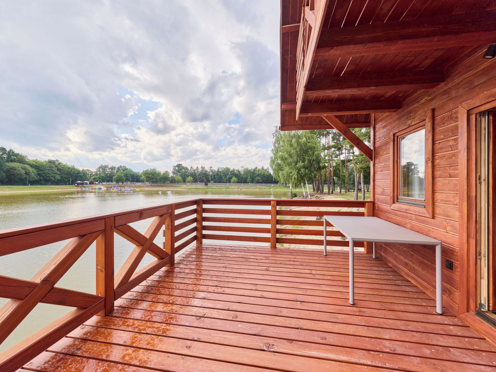 A wooden deck with a table and chairs, overlooking a lake with boats.