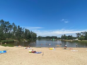 Ein Strand mit badenden und sonnenden Menschen, umgeben von Bäumen.