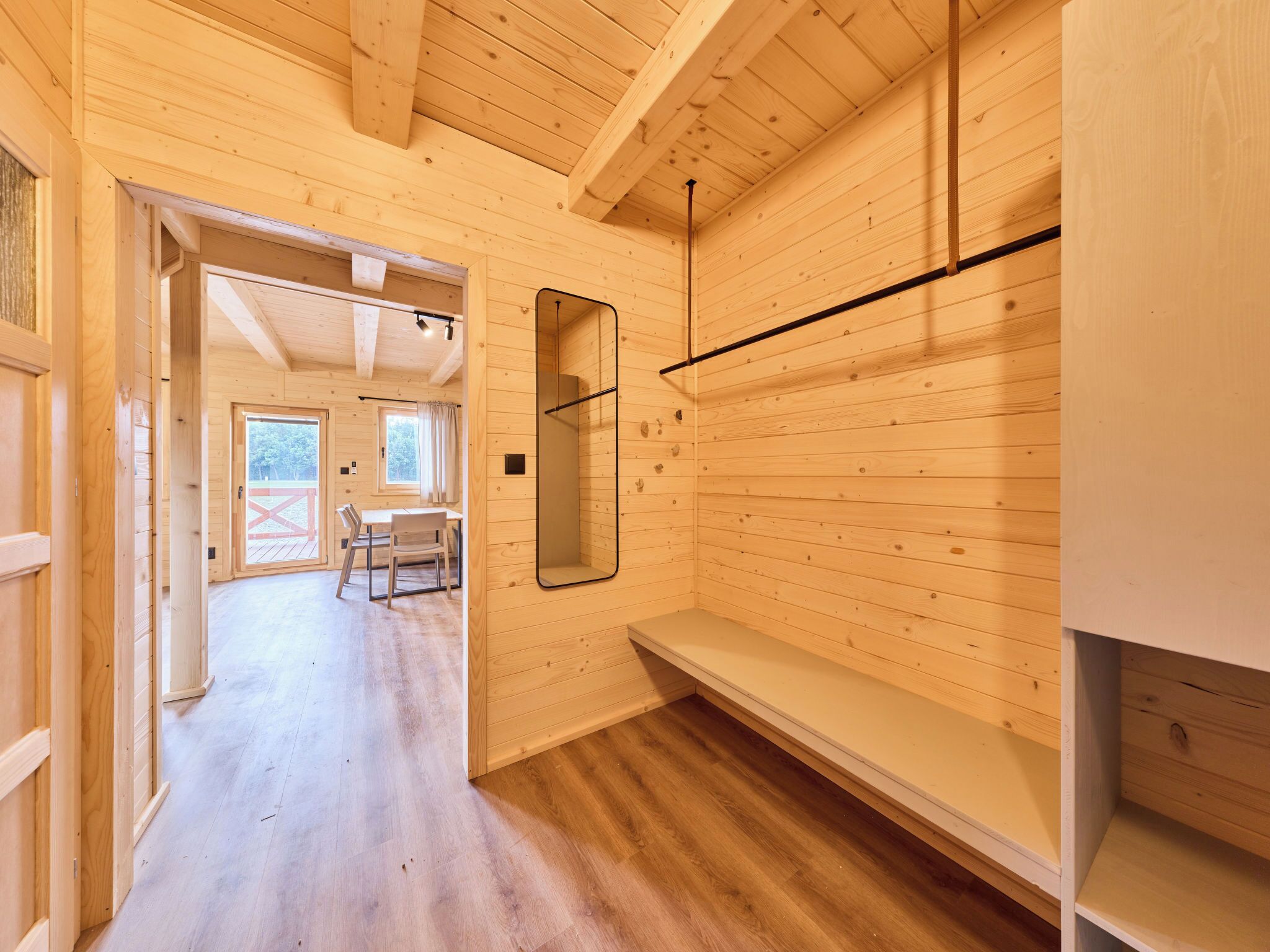 A wooden interior with a hallway leading to a dining area and a mirrored wall.