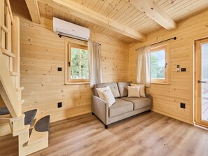Een houten blokhut van binnen met een bank, gordijnen en een airconditioning.