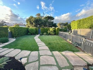 A landscaped backyard with a stone pathway, neatly trimmed hedges, and a wooden fence.