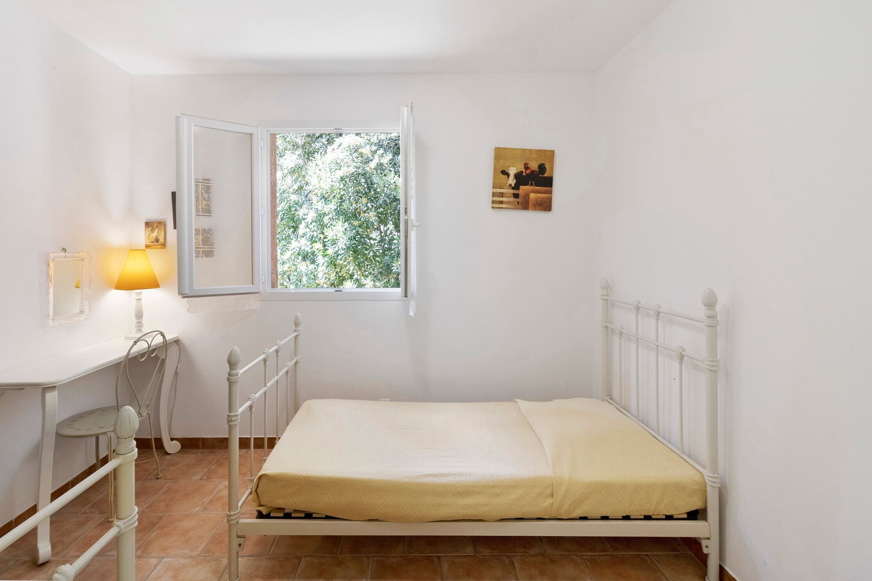 Une pièce comprenant un lit, un bureau, une chaise, une fenêtre et un tableau accroché au mur.