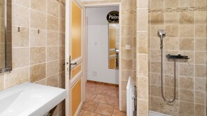 Un baño con lavamanos blanco, ducha con cabezal de ducha manual y espejo.