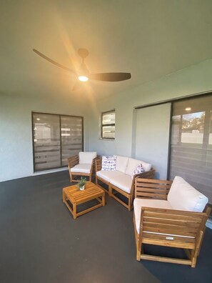 Un espacio de patio cubierto con un ventilador de techo, un sofá, dos sillones y una mesita.