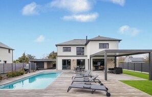 Ein modernes Haus mit Swimmingpool, Sitzgelegenheit im Freien und einer überdachten Terrasse.